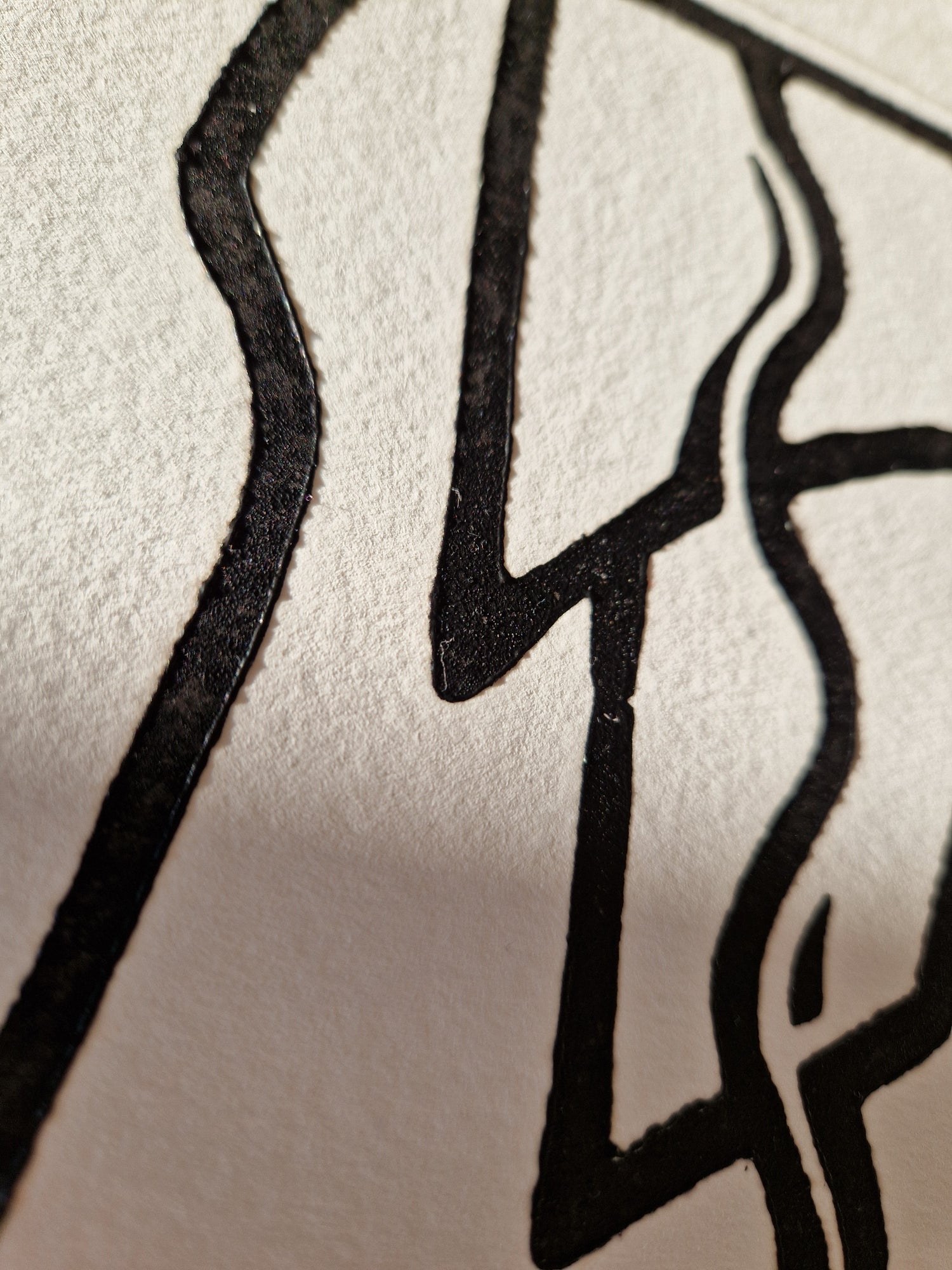 A close-up of black ink lines drawn on textured off-white paper, forming an abstract or stylized graphic.